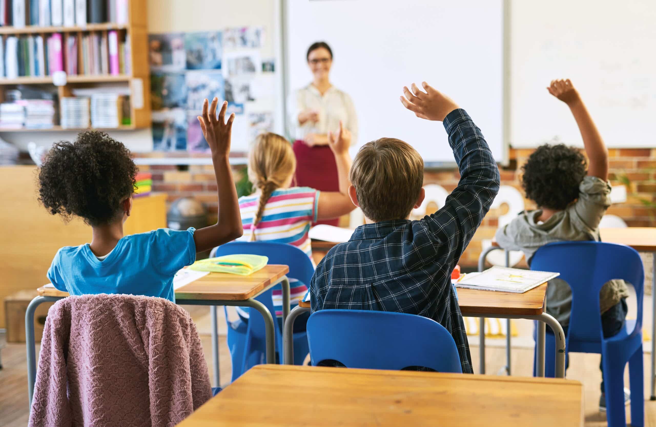 Kids raising their hands in a classroom.